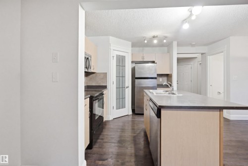 Kitchen featuring wood-finish flooring, light-toned cabinetry, stainless steel appliances, and track lighting - 3545 11 Street, Edmonton, AB - Indoor Photo Showing Kitchen With Double Sink