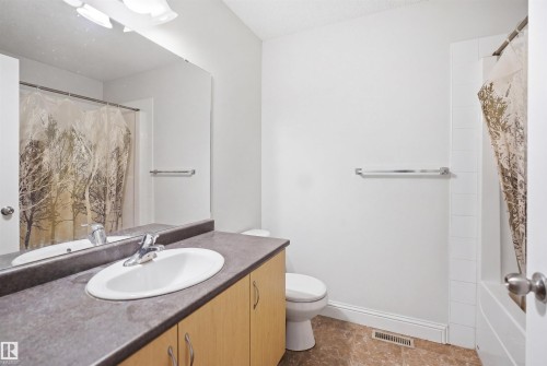 Bathroom featuring a light wood-finish vanity with an integrated sink, dark countertop, and an expansive wall-mounted mirror - 3545 11 Street, Edmonton, AB - Indoor Photo Showing Bathroom