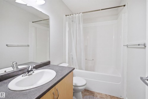 Bathroom featuring a white integrated tub and shower unit, oval sink set into a dark countertop, and light wood-finish cabinetry - 3545 11 Street, Edmonton, AB - Indoor Photo Showing Bathroom