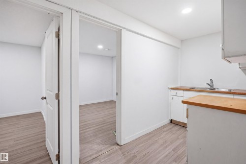 Compact kitchen area featuring wood-finish countertops, a double-basin stainless steel sink, and white cabinetry - 3545 11 Street, Edmonton, AB - Indoor