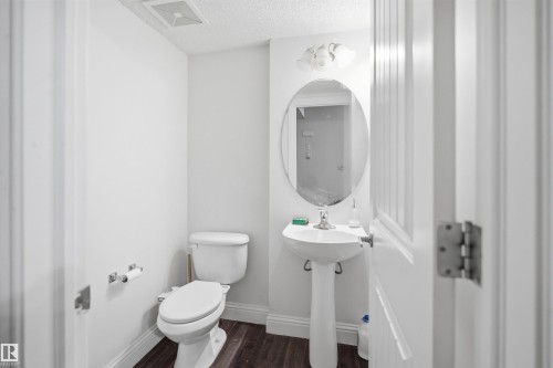 Pedestal sink with oval mirror, overhead vanity lighting, and wood-finish flooring - 3545 11 Street, Edmonton, AB - Indoor Photo Showing Bathroom