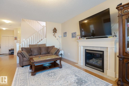 Living room featuring a gas fireplace with a tiled surround and mantel, light-toned walls, wood-finish flooring, and a staircase with white railings - 7426 Getty Way, Edmonton, AB - Indoor Photo Showing Living Room With Fireplace