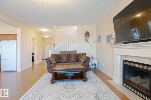 Living area featuring a fireplace with a tile surround and white mantle, light wood-finish flooring, and a white staircase with a railing - 7426 Getty Way, Edmonton, AB - Indoor Photo Showing Living Room With Fireplace