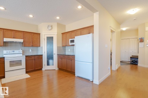 Kitchen featuring wood-finish cabinetry, dark countertops, white appliances, and a tiled backsplash - 7426 Getty Way, Edmonton, AB - Indoor Photo Showing Kitchen