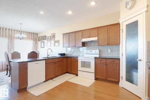 Kitchen featuring wood-finish flooring, dark stone countertops, wood cabinetry, and a white appliance suite - 7426 Getty Way, Edmonton, AB - Indoor Photo Showing Kitchen