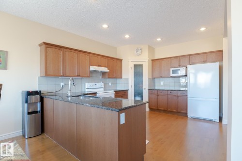 Spacious kitchen featuring a central island with a sink, light wood-finish cabinetry, granite countertops, tile backsplash, and recessed lighting - 7426 Getty Way, Edmonton, AB - Indoor Photo Showing Kitchen