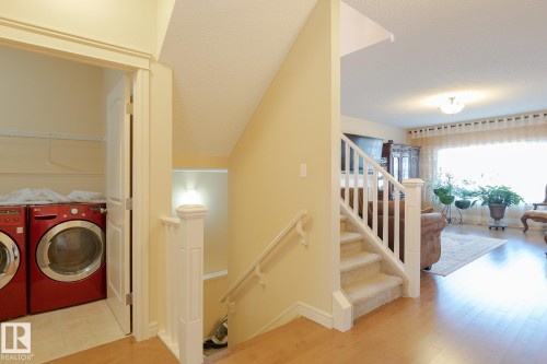 Carpeted staircase with white balusters and handrail, light wood-finish flooring, and an adjacent laundry area featuring a tile floor - 7426 Getty Way, Edmonton, AB - Indoor Photo Showing Other Room