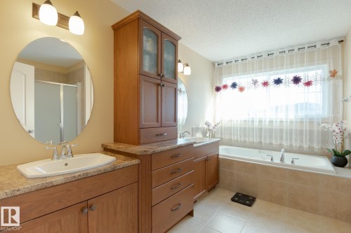 Bathroom featuring a built-in tub with surrounding tile, dual vanity with undermount sinks, wood-finish cabinetry, and overhead lighting - 7426 Getty Way, Edmonton, AB - Indoor Photo Showing Bathroom