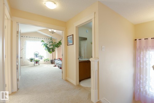 Carpeted hallway with a flush mount ceiling light, leading to a room with a vaulted ceiling and large window, and an adjacent bathroom featuring a vanity with a white basin - 7426 Getty Way, Edmonton, AB - Indoor Photo Showing Other Room