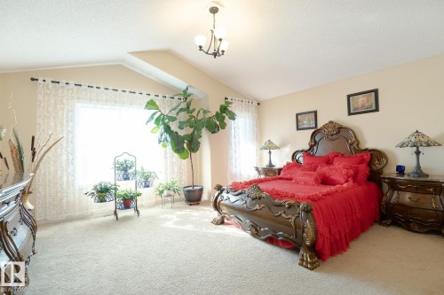 Vaulted ceiling with an overhead chandelier, large window with decorative curtains, and plush carpeting throughout - 7426 Getty Way, Edmonton, AB - Indoor Photo Showing Bedroom