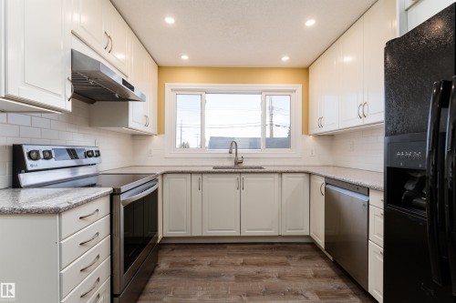U-shaped kitchen featuring white shaker cabinetry, speckled countertops, a subway tile backsplash, stainless steel appliances, and wood-finish flooring - 13331 64 Street Nw, Edmonton, AB - Indoor Photo Showing Kitchen With Upgraded Kitchen