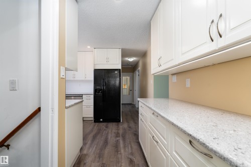Kitchen featuring white shaker-style cabinetry, light-toned countertops, a black refrigerator, and wood-finish flooring - 13331 64 Street Nw, Edmonton, AB - Indoor Photo Showing Kitchen