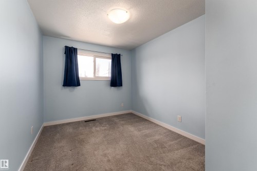 Carpeted room featuring light blue walls, white trim, and a double window with dark blue curtains - 13331 64 Street Nw, Edmonton, AB - Indoor Photo Showing Other Room