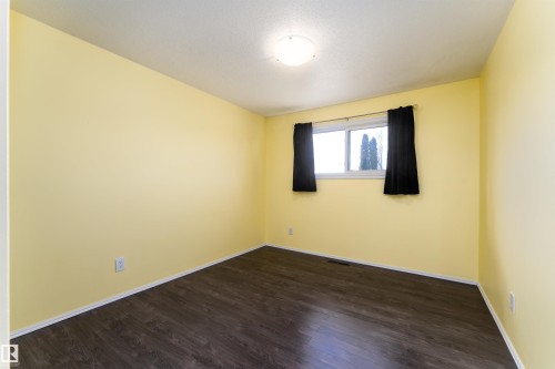 Spacious interior room featuring wood-finish flooring, light yellow walls, and a white baseboard trim - 13331 64 Street Nw, Edmonton, AB - Indoor Photo Showing Other Room