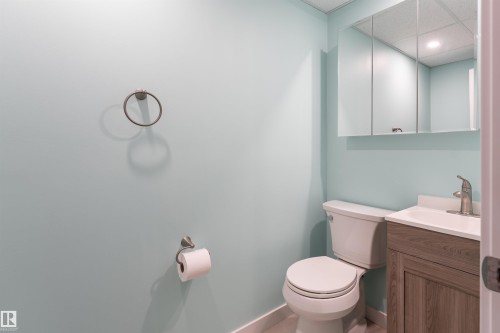 Bathroom featuring a wood-finish vanity with an integrated sink, a medicine cabinet with mirrored doors, a toilet, and light blue walls - 13331 64 Street Nw, Edmonton, AB - Indoor Photo Showing Bathroom