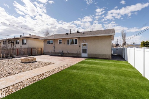 Expansive rear yard featuring an artificial turf lawn, a concrete patio, and a stone fire pit area - 13331 64 Street Nw, Edmonton, AB - Outdoor