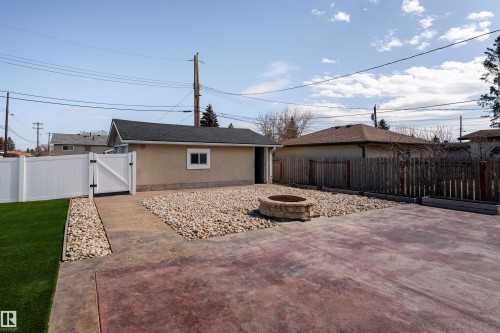 Rear yard featuring a fire pit with stone surround, a section of artificial turf, and a white vinyl privacy fence with gate - 13331 64 Street Nw, Edmonton, AB - Outdoor