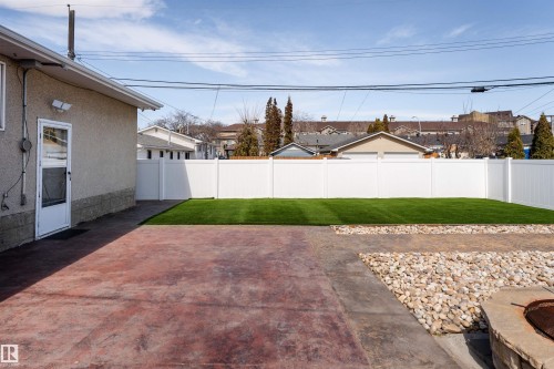 Private backyard featuring a vibrant artificial turf lawn, white vinyl fencing, a concrete patio, and a stone-edged fire pit - 13331 64 Street Nw, Edmonton, AB - Outdoor
