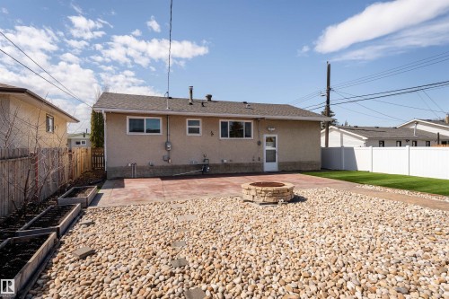 Rear exterior featuring a concrete patio, stone fire pit, pebble landscaping, artificial turf, and raised garden beds - 13331 64 Street Nw, Edmonton, AB - Outdoor