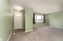 Entryway leading into a living space featuring light green walls, a white front door with an arched glass insert, ceiling-mounted light fixture, gray carpeting, and a large window with dark curtains - 13331 64 Street Nw, Edmonton, AB  - Indoor Photo Showing Other Room 