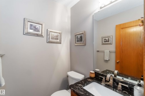 Bathroom featuring a white toilet, black patterned countertop, integrated rectangular sink, brushed nickel faucet, and a large wall-mounted mirror - 17224 83 Street, Edmonton, AB - Indoor Photo Showing Bathroom