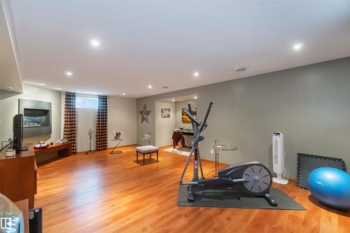 Spacious finished basement with wood-finish flooring, recessed lighting, and a modern wall-mounted fireplace - 17224 83 Street, Edmonton, AB - Indoor Photo Showing Gym Room