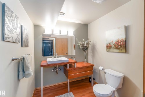 Bathroom featuring a wood-finish vanity with an integrated rectangular sink, a wall-mounted mirror, and wood-finish flooring - 17224 83 Street, Edmonton, AB - Indoor Photo Showing Bathroom