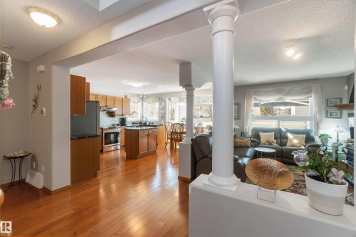 Open-concept interior featuring wood-finish flooring, a kitchen with wood cabinetry and stainless steel appliances, a kitchen island with dark countertops, a dining area with a window, and a living area with a large window - 17224 83 Street, Edmonton, AB - Indoor
