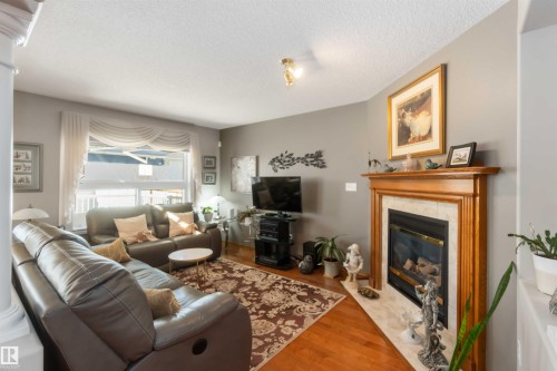 Living area featuring wood-finish flooring, a fireplace with a light-toned wood mantel and tile surround, and a large window providing natural light - 17224 83 Street, Edmonton, AB - Indoor Photo Showing Living Room With Fireplace