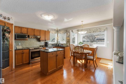 Kitchen featuring wood-finish cabinetry, stainless steel appliances, a center island with a dark countertop, and light wood-finish flooring - 17224 83 Street, Edmonton, AB - Indoor