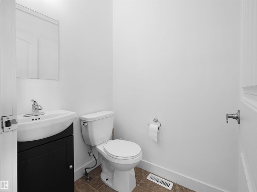 The bathroom features a modern vanity with a white basin and chrome faucet, a white toilet, and a wall-mounted mirror - #11 13215 153 Avenue, Edmonton, AB - Indoor Photo Showing Bathroom