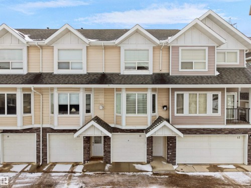 This property features a multi-level design with light-colored siding, a dark roof, and individual garage access for each unit - #11 13215 153 Avenue, Edmonton, AB - Outdoor With Facade