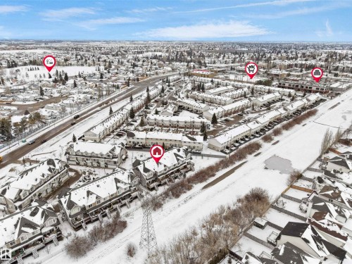 This aerial view highlights the property within a community featuring numerous residential structures, including townhomes and houses, all blanketed in snow - #11 13215 153 Avenue, Edmonton, AB - Outdoor With View