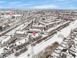This aerial view highlights the property within a community featuring numerous residential structures, including townhomes and houses, all blanketed in snow - 