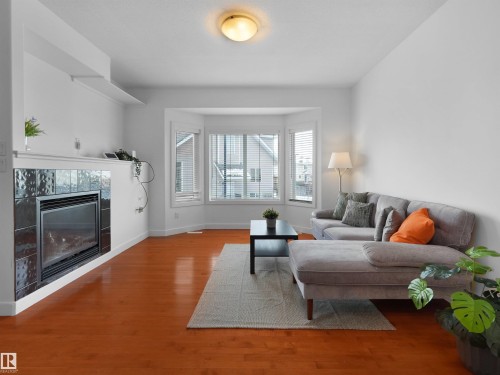 Living room featuring hardwood floors, a fireplace with dark tile surround, and a bay window providing natural light - #11 13215 153 Avenue, Edmonton, AB - Indoor Photo Showing Living Room With Fireplace