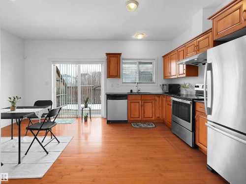 This kitchen features wood flooring, wooden cabinetry, and stainless steel appliances including a refrigerator, oven, and dishwasher - #11 13215 153 Avenue, Edmonton, AB - Indoor Photo Showing Kitchen With Double Sink