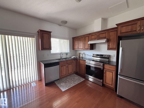 Kitchen featuring wood-finish flooring, dark stone countertops, wood cabinetry, and stainless steel appliances - #11 13215 153 Avenue, Edmonton, AB - Indoor Photo Showing Kitchen