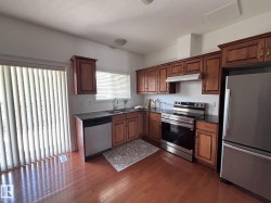 Kitchen featuring wood-finish flooring, dark stone countertops, wood cabinetry, and stainless steel appliances - 