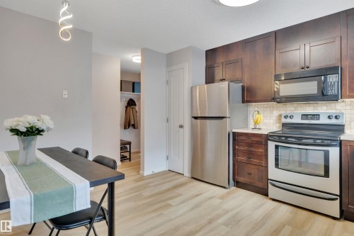 The kitchen features dark wood cabinetry, stainless steel appliances, and a tiled backsplash - 585 Knottwood Road W, Edmonton, AB - Indoor Photo Showing Kitchen