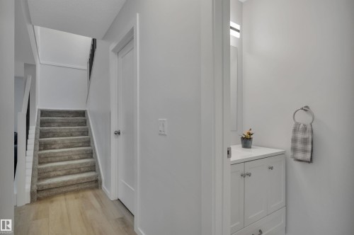This inviting entryway features light wood flooring, a carpeted staircase with white risers, and a white vanity with a light-colored countertop - 585 Knottwood Road W, Edmonton, AB - Indoor Photo Showing Other Room