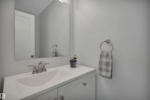 Bathroom vanity with a white countertop and an integrated sink, brushed nickel faucet, and a wall-mounted mirror - 585 Knottwood Road W, Edmonton, AB - Indoor Photo Showing Bathroom