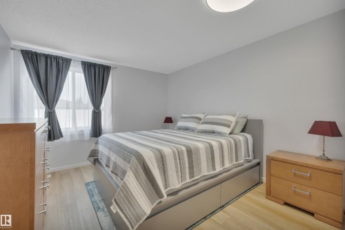 This bedroom features light wood-style flooring, light gray walls, and a window with both sheer and blackout curtains - 585 Knottwood Road W, Edmonton, AB - Indoor Photo Showing Bedroom