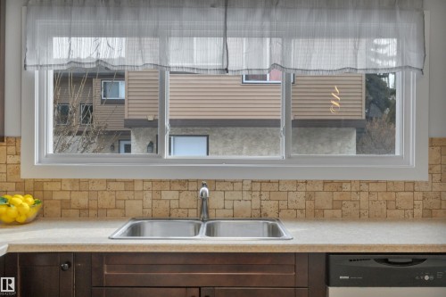 The kitchen features a double basin stainless steel sink, light-colored countertops, and dark wood cabinetry - 585 Knottwood Road W, Edmonton, AB - Indoor Photo Showing Kitchen With Double Sink