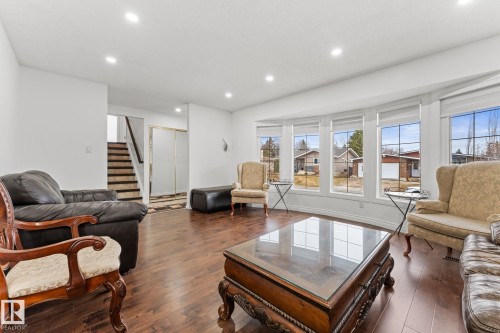 Spacious living area featuring expansive bay windows, wood-finish flooring, recessed lighting, white walls, and a staircase with striped runners - 16424 106 Street, Edmonton, AB - Indoor Photo Showing Living Room