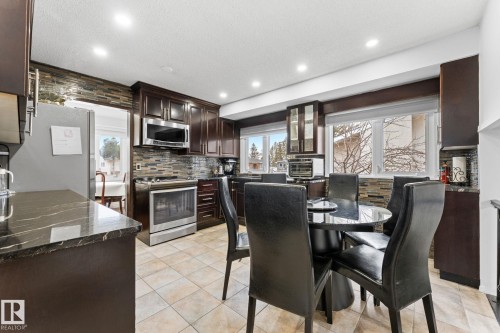 Kitchen featuring dark wood cabinetry, stainless steel appliances, stacked stone backsplash, dark countertops, and recessed lighting - 16424 106 Street, Edmonton, AB - Indoor