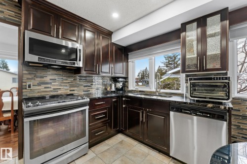 Kitchen featuring dark wood cabinetry, stainless steel appliances, a mosaic tile backsplash, and stone countertops - 16424 106 Street, Edmonton, AB - Indoor Photo Showing Kitchen With Upgraded Kitchen