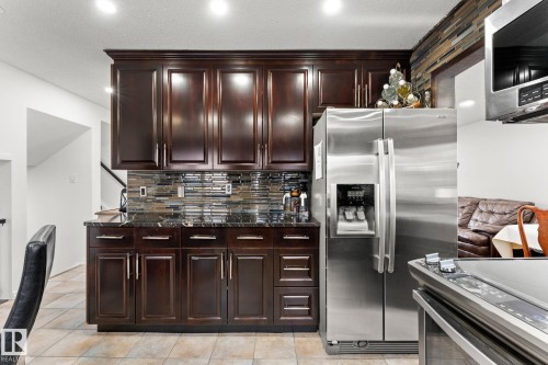 Kitchen featuring dark wood cabinetry, a mosaic tile backsplash, black stone countertops, stainless steel appliances, and recessed lighting - 16424 106 Street, Edmonton, AB - Indoor Photo Showing Kitchen With Upgraded Kitchen