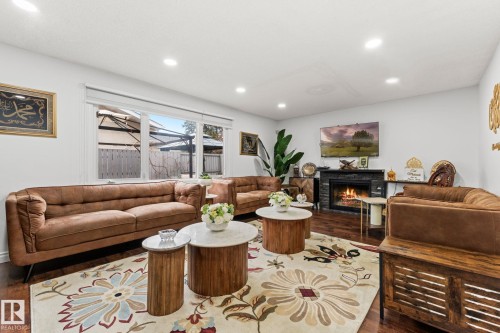 Spacious living area featuring rich wood-finish flooring, a contemporary fireplace with a dark stone surround, and multiple recessed ceiling lights - 16424 106 Street, Edmonton, AB - Indoor Photo Showing Other Room With Fireplace