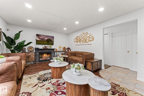 Living space featuring wood-finish flooring, a stacked stone fireplace, recessed lighting, and a white paneled door - 16424 106 Street, Edmonton, AB - Indoor Photo Showing Other Room With Fireplace