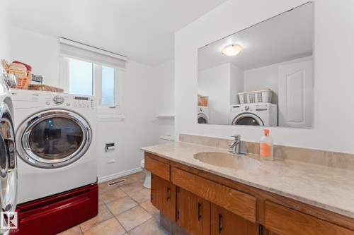 Bathroom featuring a wood-finish vanity with an integrated sink and a light-toned countertop, a wall-mounted mirror, and tile flooring - 16424 106 Street, Edmonton, AB - Indoor Photo Showing Laundry Room